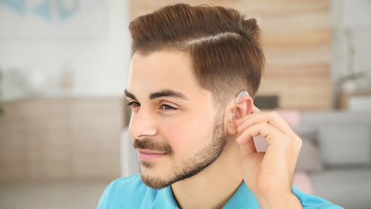 Person wearing a modern hearing aid, smiling and engaged in conversation with friends at a dinner table.