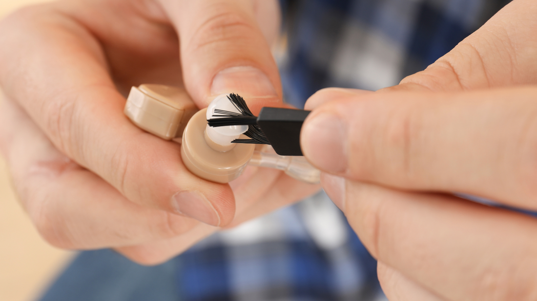 A person carefully cleaning a hearing aid with a small brush