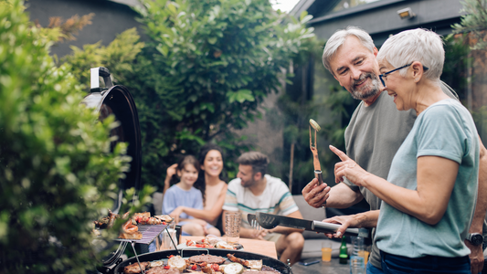 Family gathering with people chatting around a table and a grill in the background.