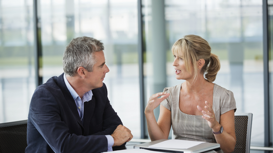 Two people sitting at a table engaged in conversation, one person is listening intently while the other speaks, representing low-tech exercises to improve hearing comprehension.