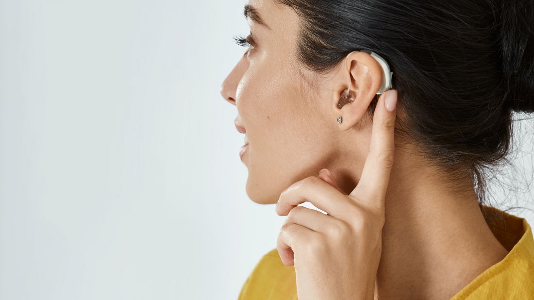 A person adjusting a hearing aid, looking satisfied with improved hearing.