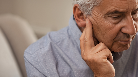 An elderly person with a concerned expression holding their hand to their ear, symbolizing hearing loss.