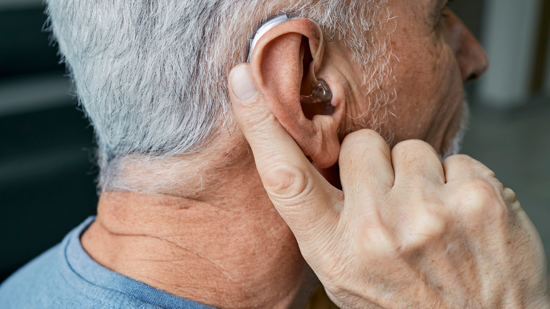 A person adjusting a small hearing aid device behind their ear