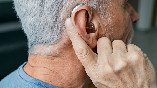 A person adjusting a small hearing aid device behind their ear