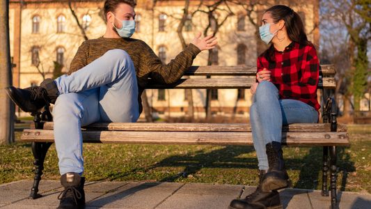 Two people having a conversation outdoors at a table with a potted plant, representing safer ways to socialize during the pandemic