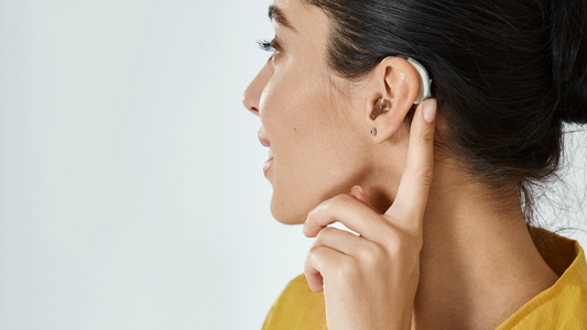 Illustration showing a person gently placing a hearing aid above their ear with one hand, and then another person smoothly removing a hearing aid from behind their ear with two fingers.